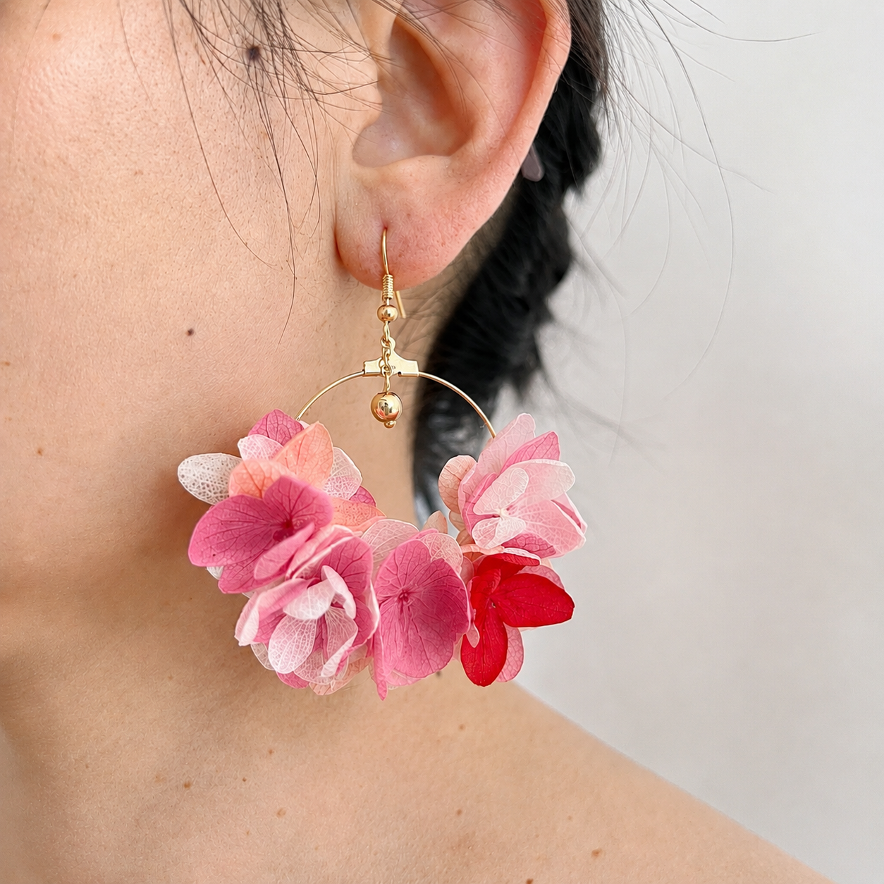 Détail des pétales d'hortensias stabilisés roses sur créoles dorées.