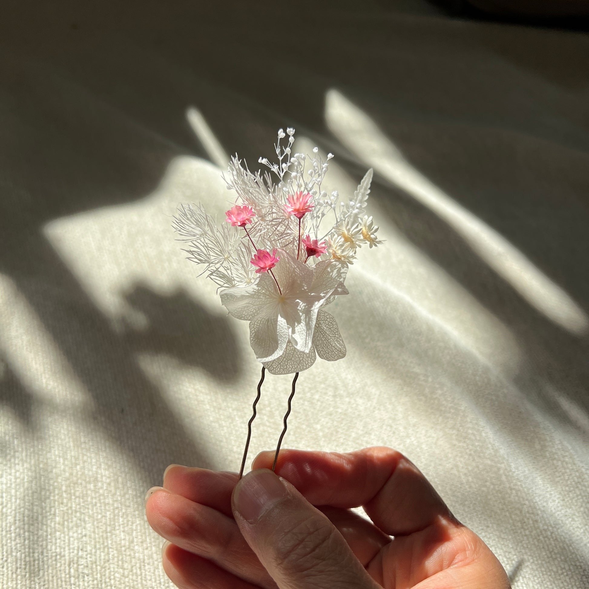 Épingles en fleurs stabilisées rose poudré et blanc présentées à la lumière naturelle
