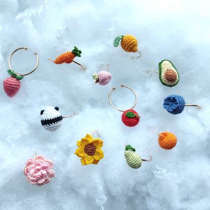 Bague en crochet fait main représentant des fruits et des fleurs colorés, dont une fraise, une carotte, un avocat, un tournesol et plus encore, sur un fond de nuages blancs