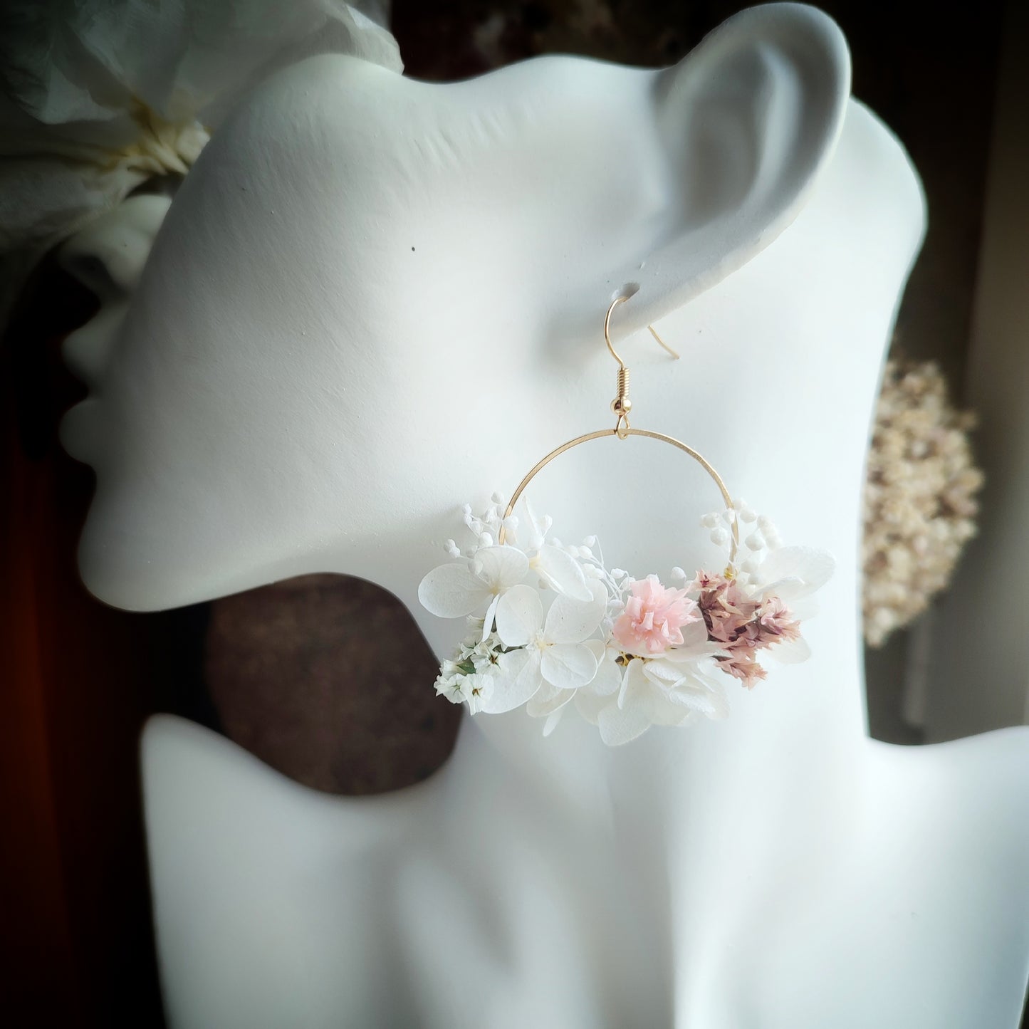 Boucles d'oreilles florales Clara portées, montrant des fleurs éternelles blanches et roses délicatement disposées sur une créole dorée.