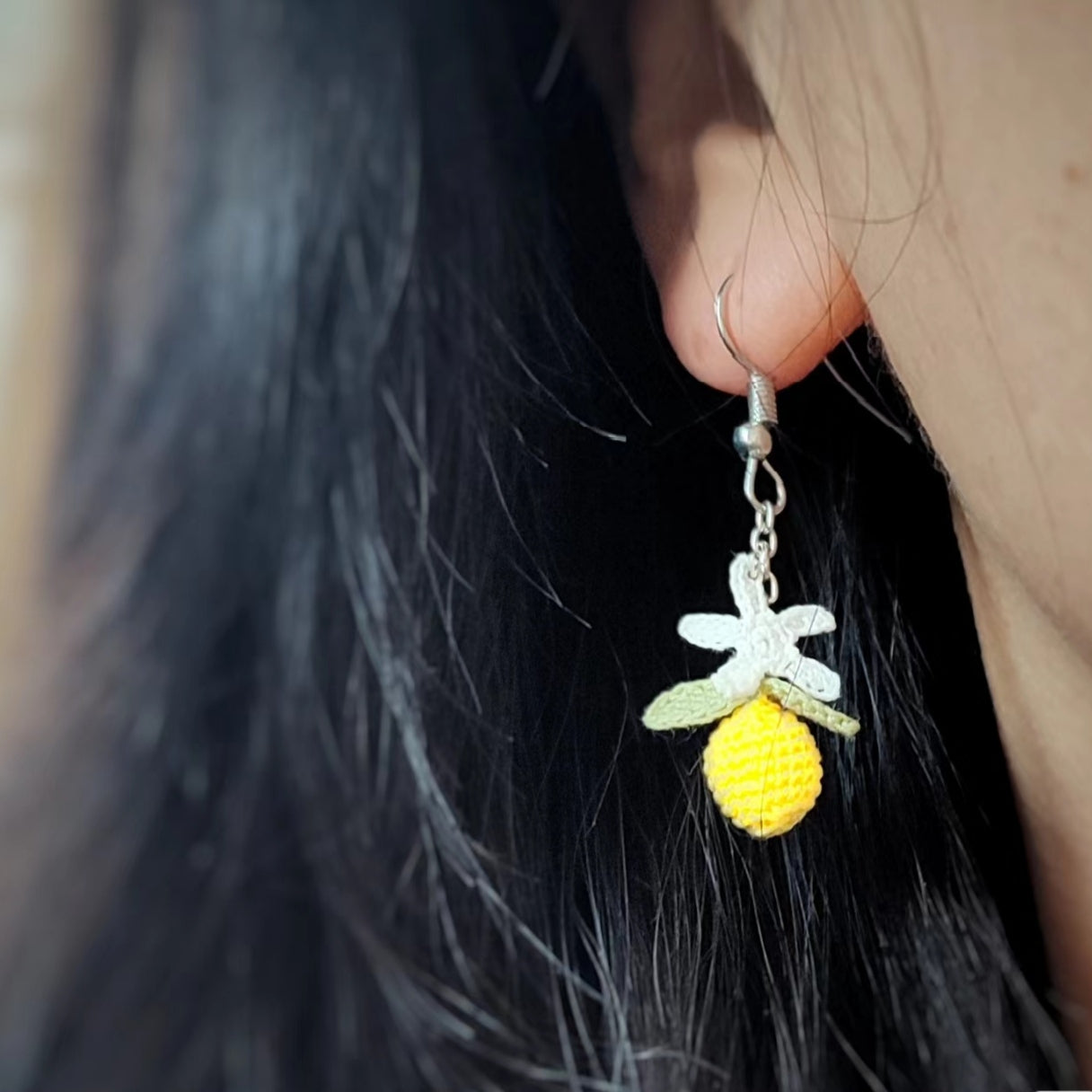 une boucle d'oreille en crochet fait main en forme de citron miniature avec une fleur de citronnier, un accessoire original et frais.