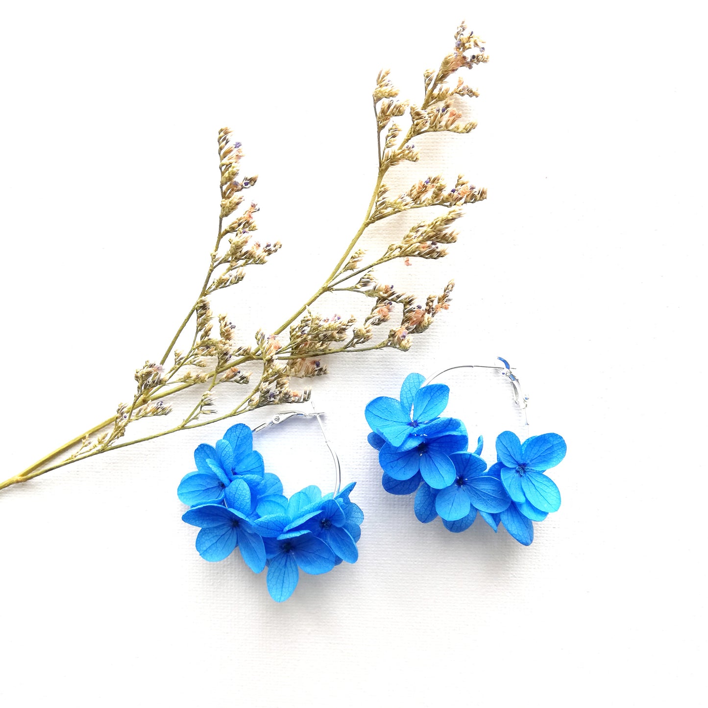 Vue rapprochée de boucles d'oreilles créoles en fleurs bleues, fabriquées à la main avec des fleurs stabilisées, un accessoire unique pour un look frais et nature