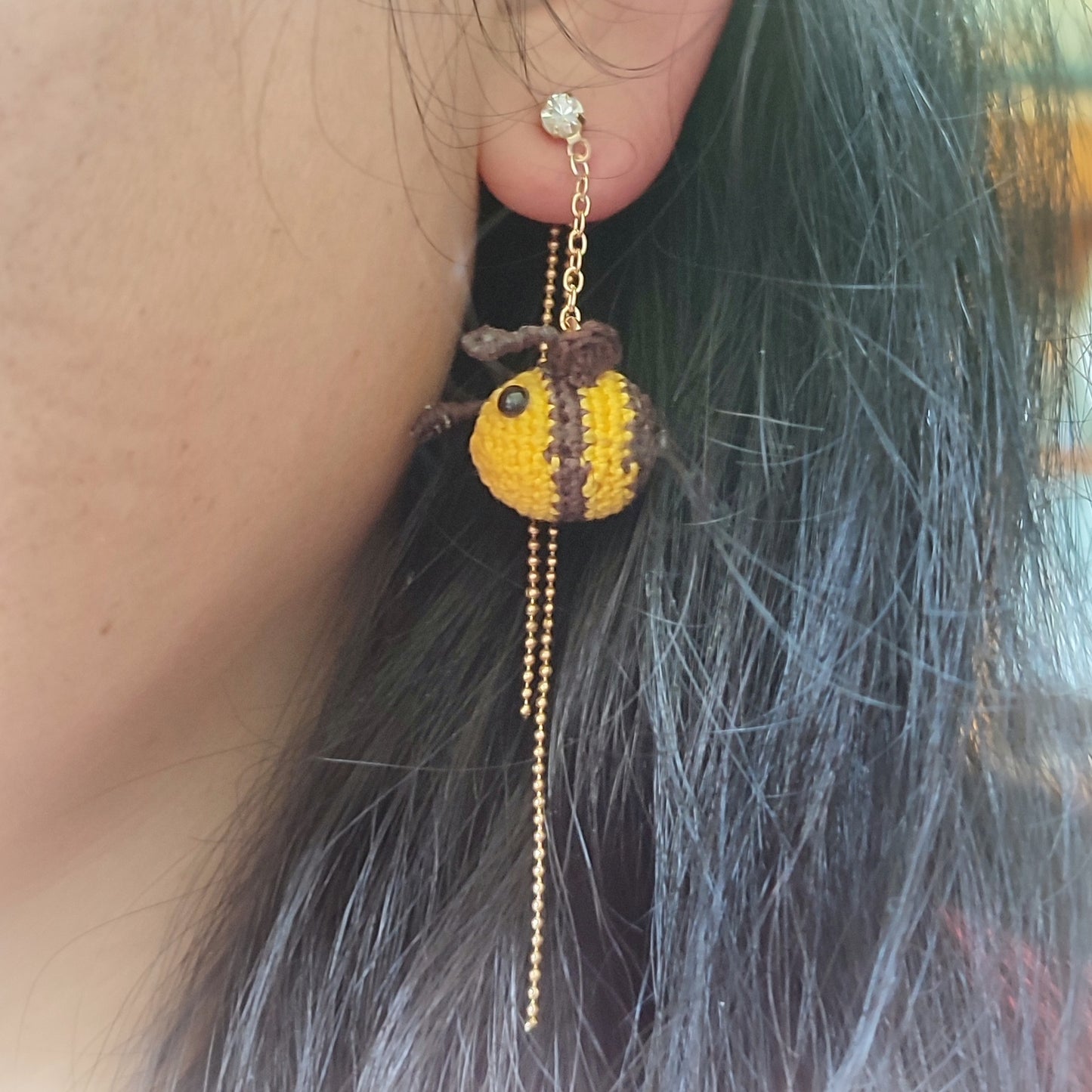 Boucles d'oreilles abeille en crochet suspendues à une chaîne dorée, portées sur une oreille.