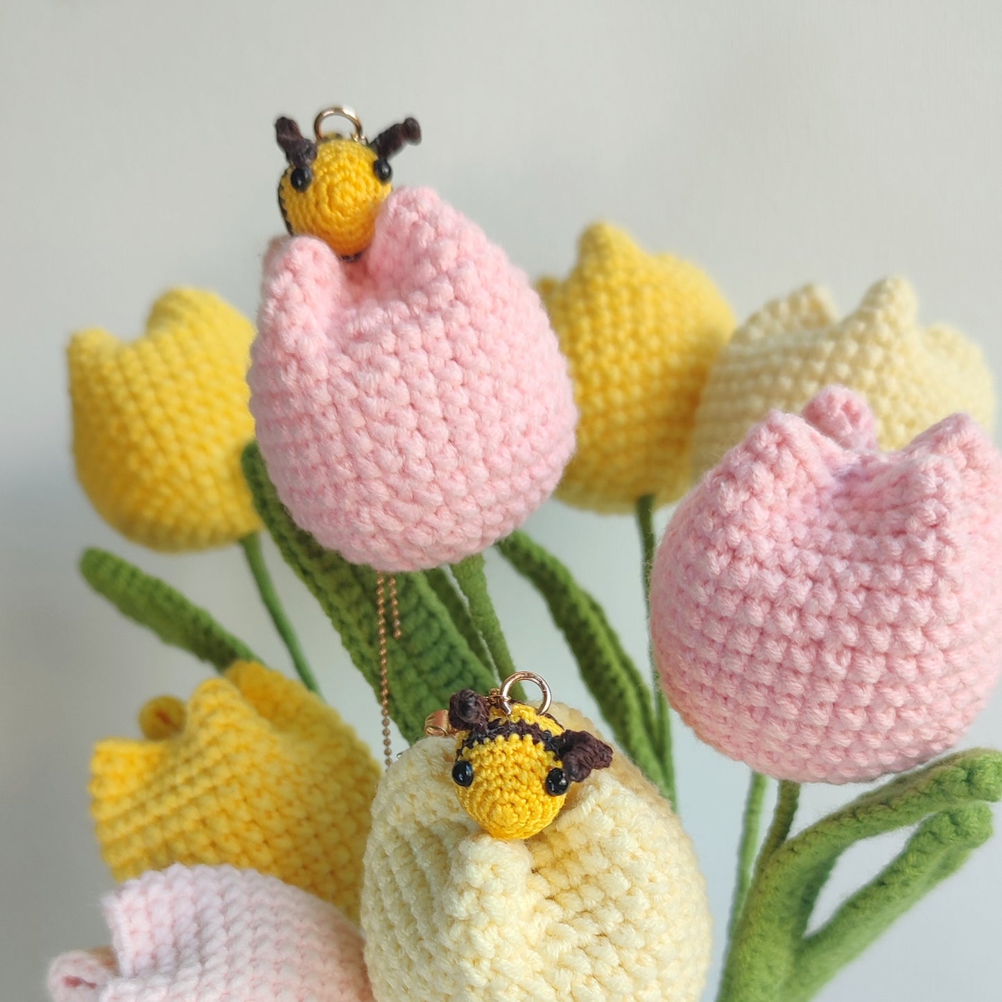 Deux boucles d'oreilles abeille en crochet, une suspendue à une chaîne dorée et l'autre à une tulipe crochetée.