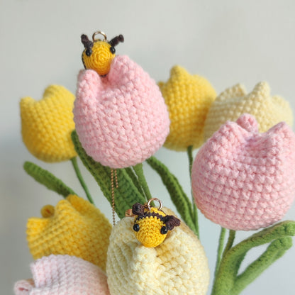 Deux boucles d'oreilles abeille en crochet, une suspendue à une chaîne dorée et l'autre à une tulipe crochetée.