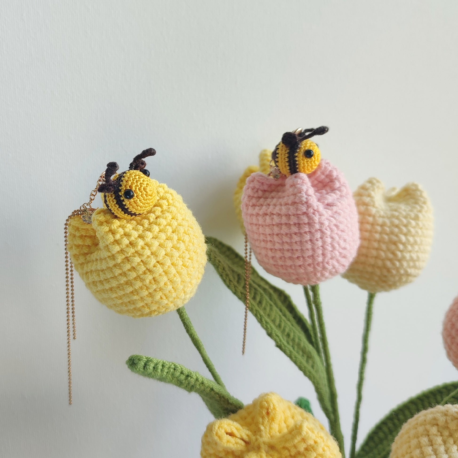 Deux boucles d'oreilles abeille en crochet, une suspendue à une chaîne dorée et l'autre à une tulipe crochetée.