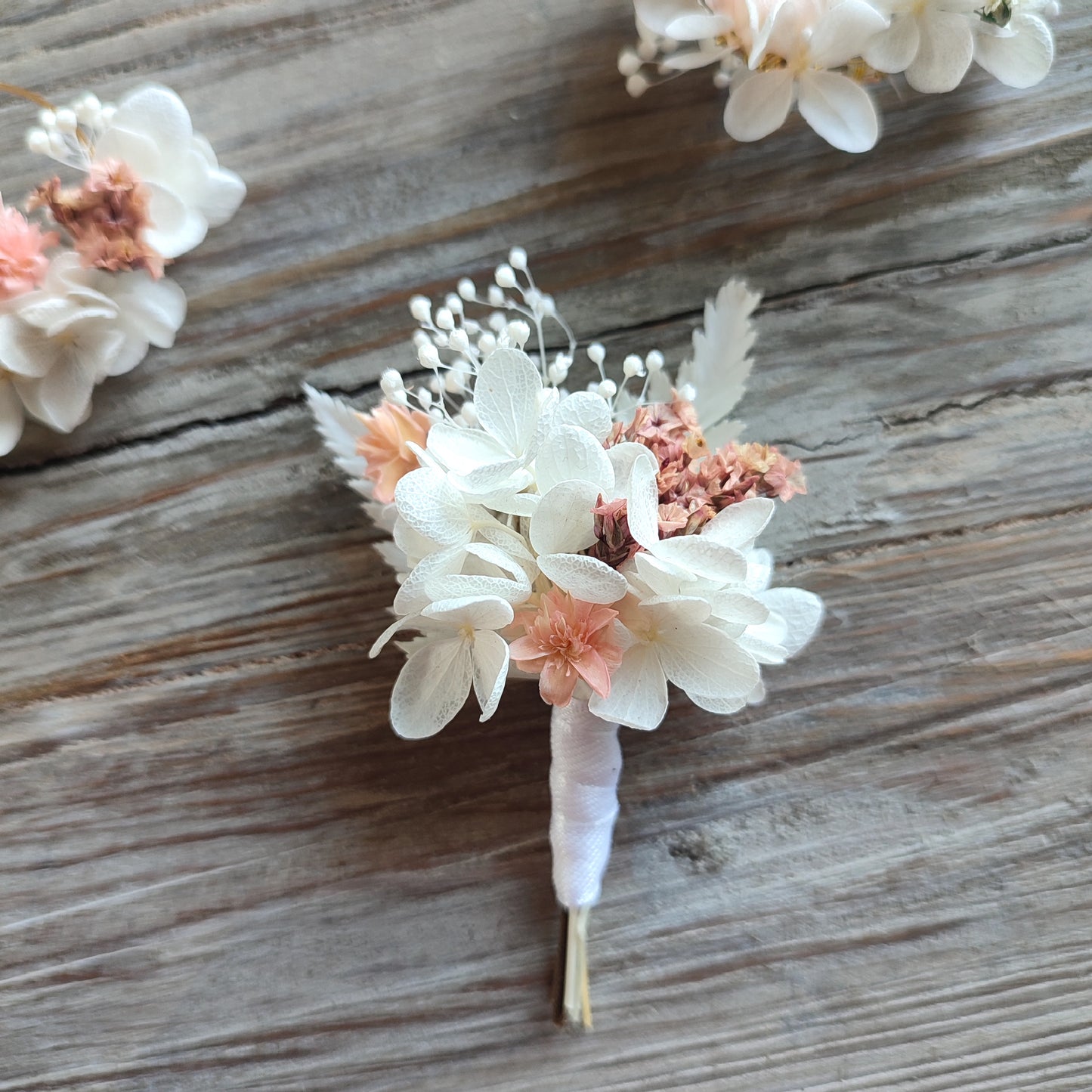 Boutonnière florale Clara en gros plan, montrant des détails des fleurs éternelles blanches et roses.