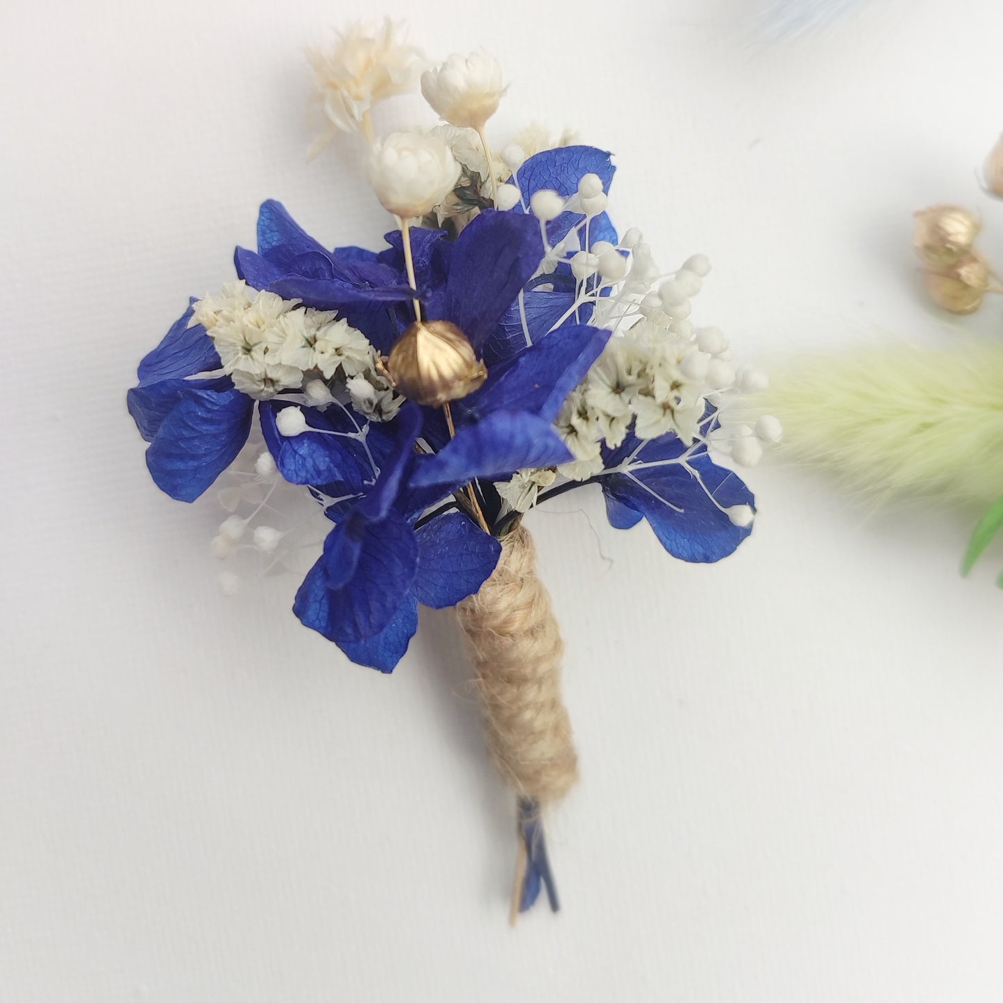 Boutonnière florale bleu foncé avec des fleurs de gypsophile et des détails dorés.