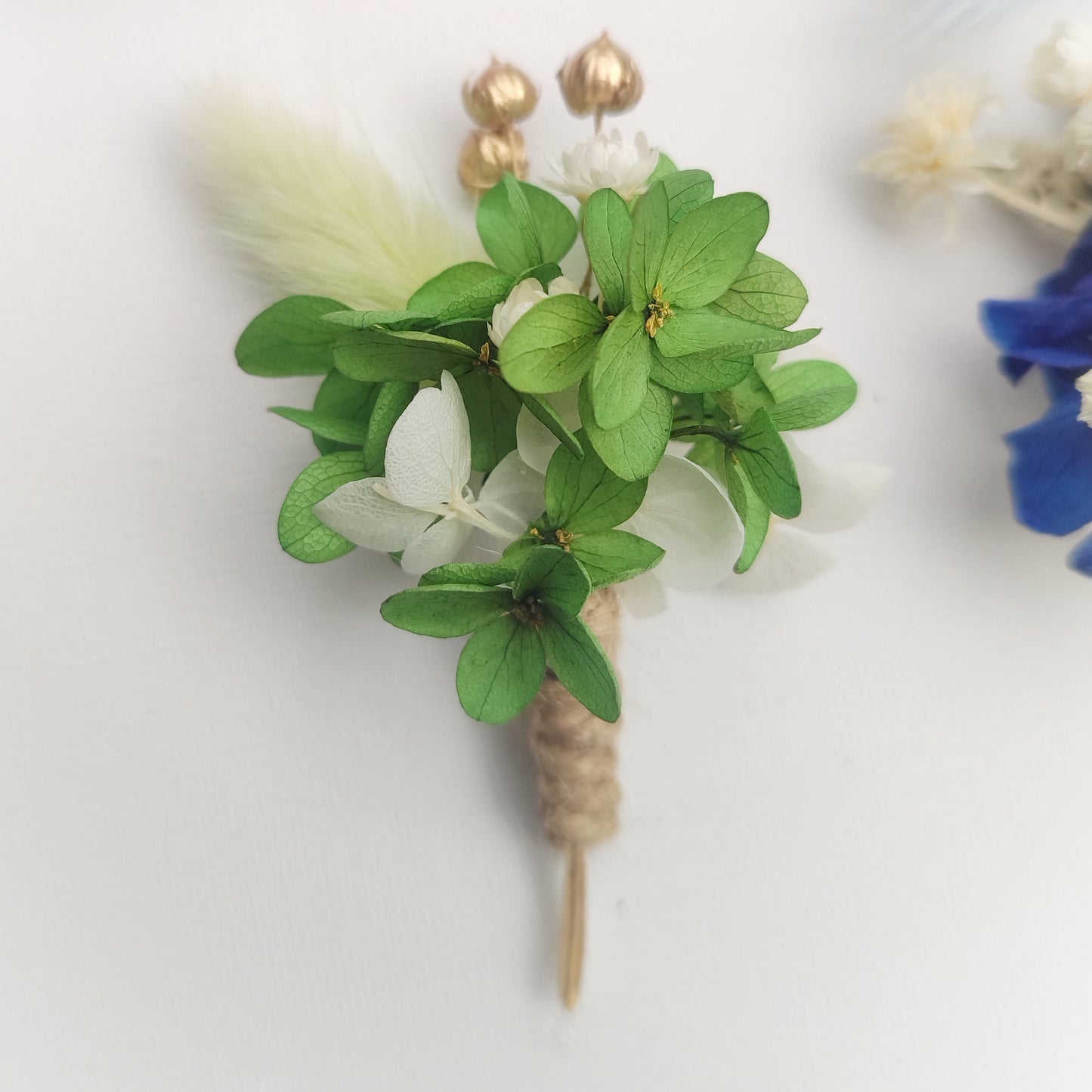Boutonnière florale verte avec des petites fleurs blanches et une plume décorative.