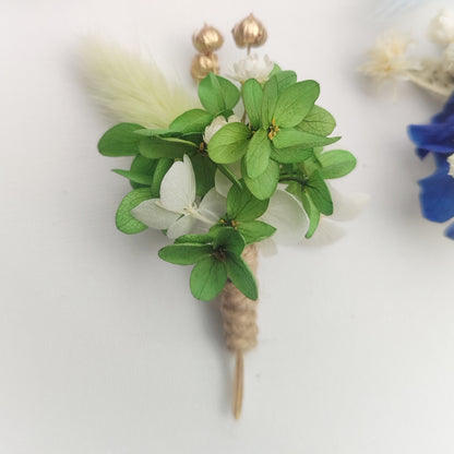 Boutonnière florale verte avec des petites fleurs blanches et une plume décorative.