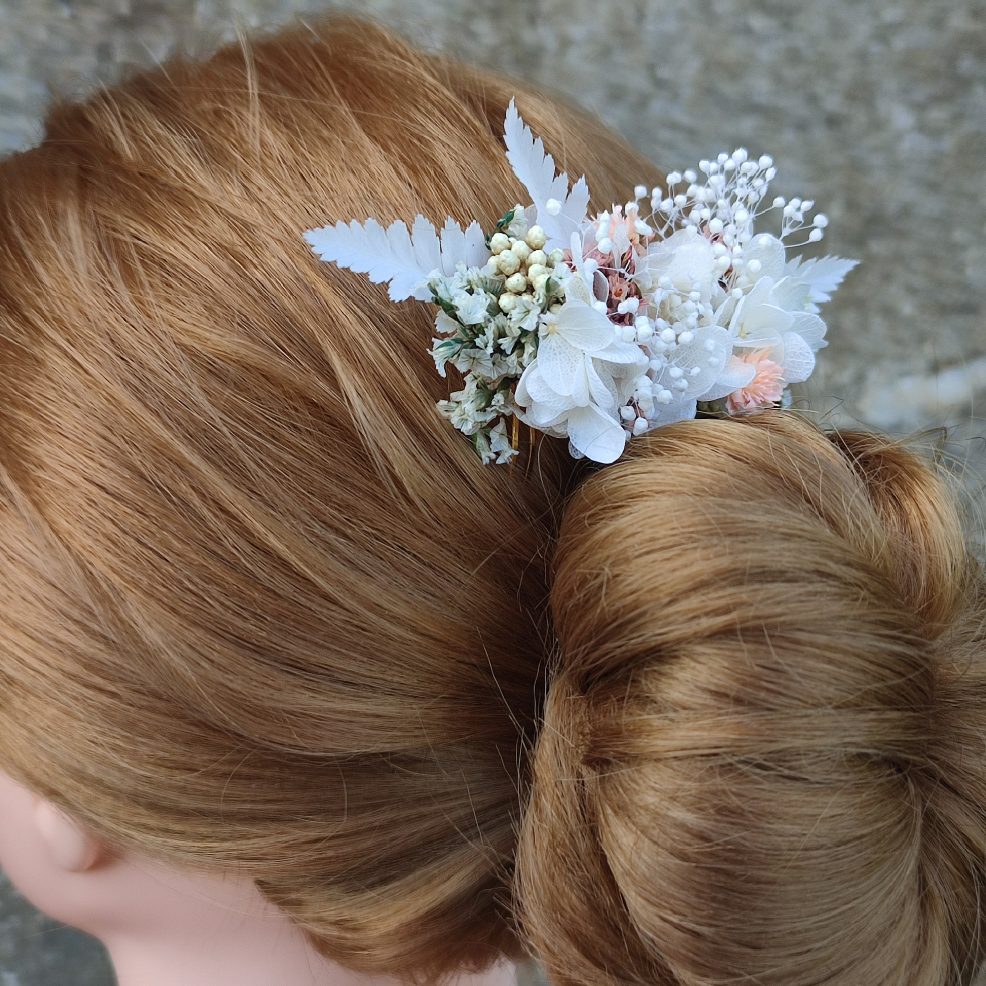 Peigne floral Clara avec des fleurs éternelles blanches et roses, inséré dans une coiffure élégante.