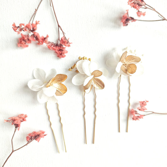 Lot de 3 épingles à cheveux "Éclat Floréal Alcina" ornées de fleurs stabilisées blanches et dorées, disposées sur un fond blanc.