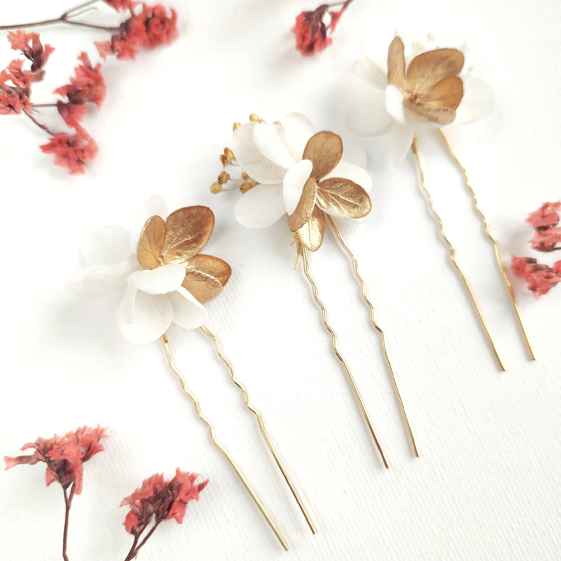 Lot de 3 épingles à cheveux "Éclat Floréal Alcina" ornées de fleurs stabilisées blanches et dorées, disposées sur un fond blanc.
