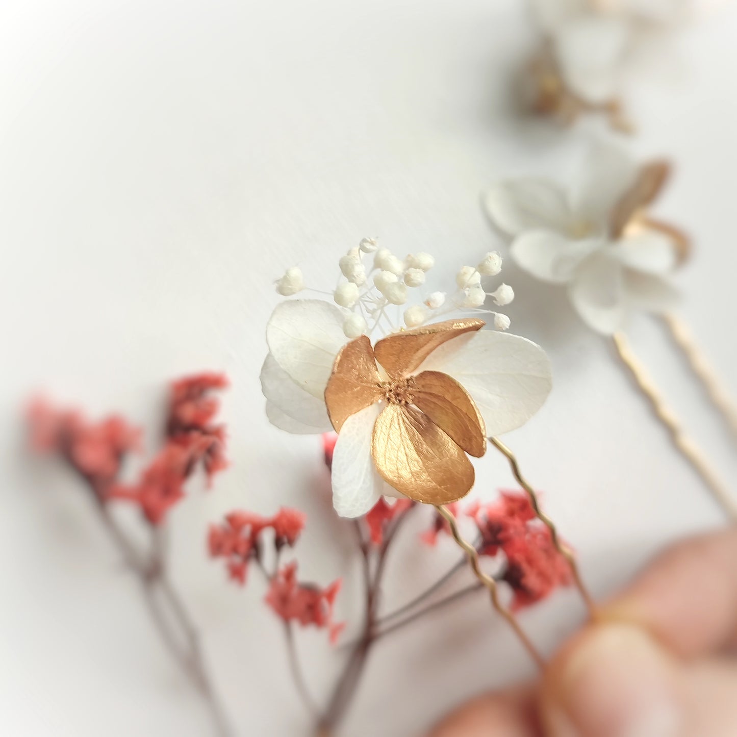 Détail des épingles à cheveux "Éclat Floréal Alcina" montrant les fleurs stabilisées blanches et dorées et leur finition artisanale.