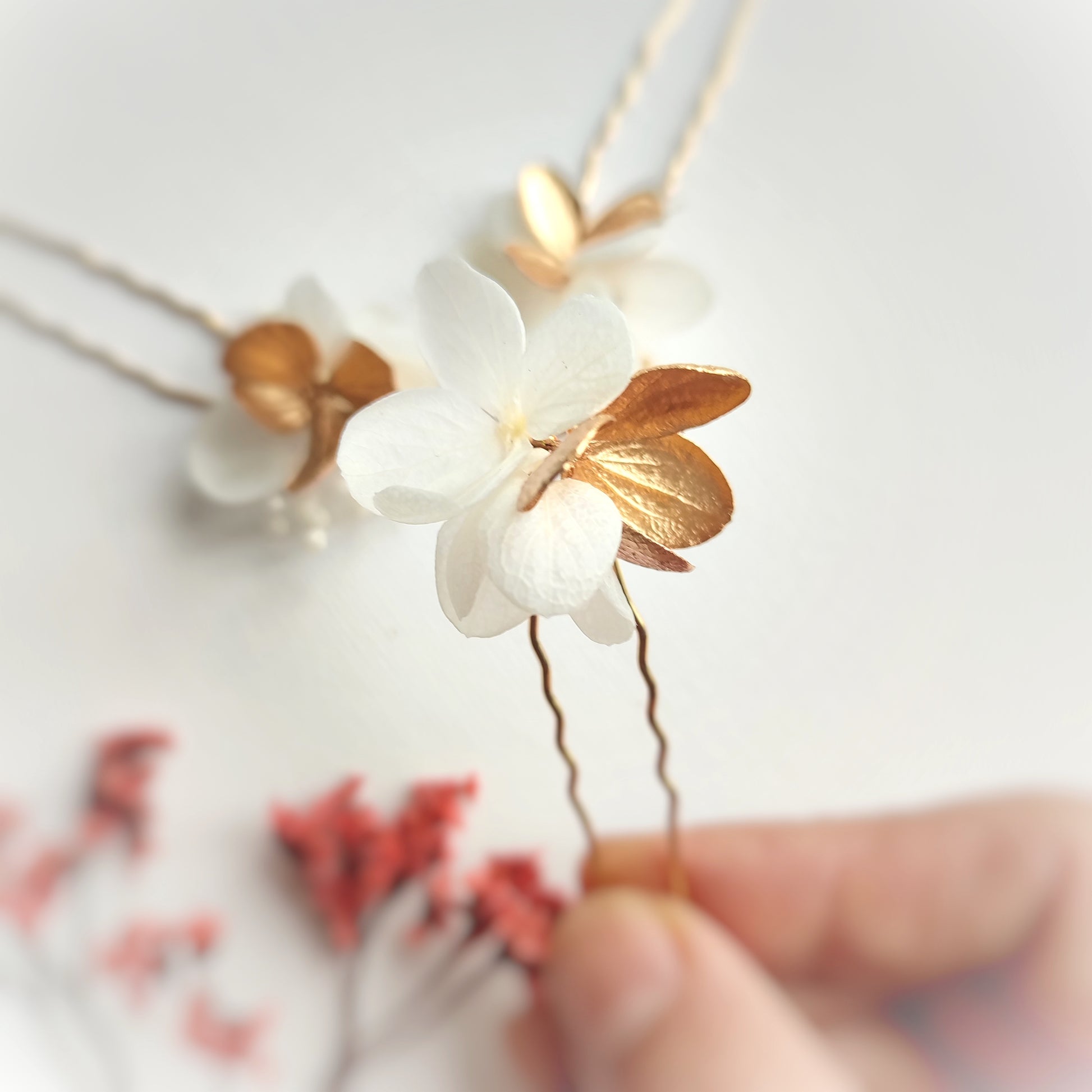 Détail des épingles à cheveux "Éclat Floréal Alcina" montrant les fleurs stabilisées blanches et dorées et leur finition artisanale.