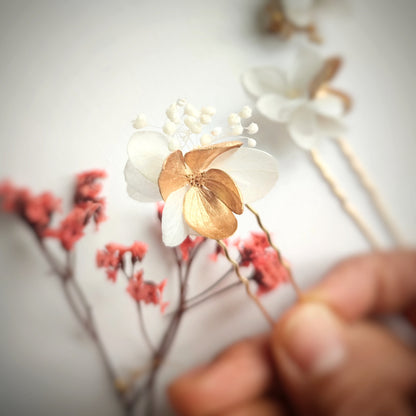 Détail des épingles à cheveux "Éclat Floréal Alcina" montrant les fleurs stabilisées blanches et dorées et leur finition artisanale.
