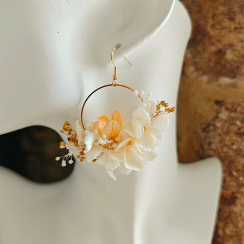 Boucle d’oreille créole faite main, fleurs séchées blanches et champagne portée sur un buste blanc.