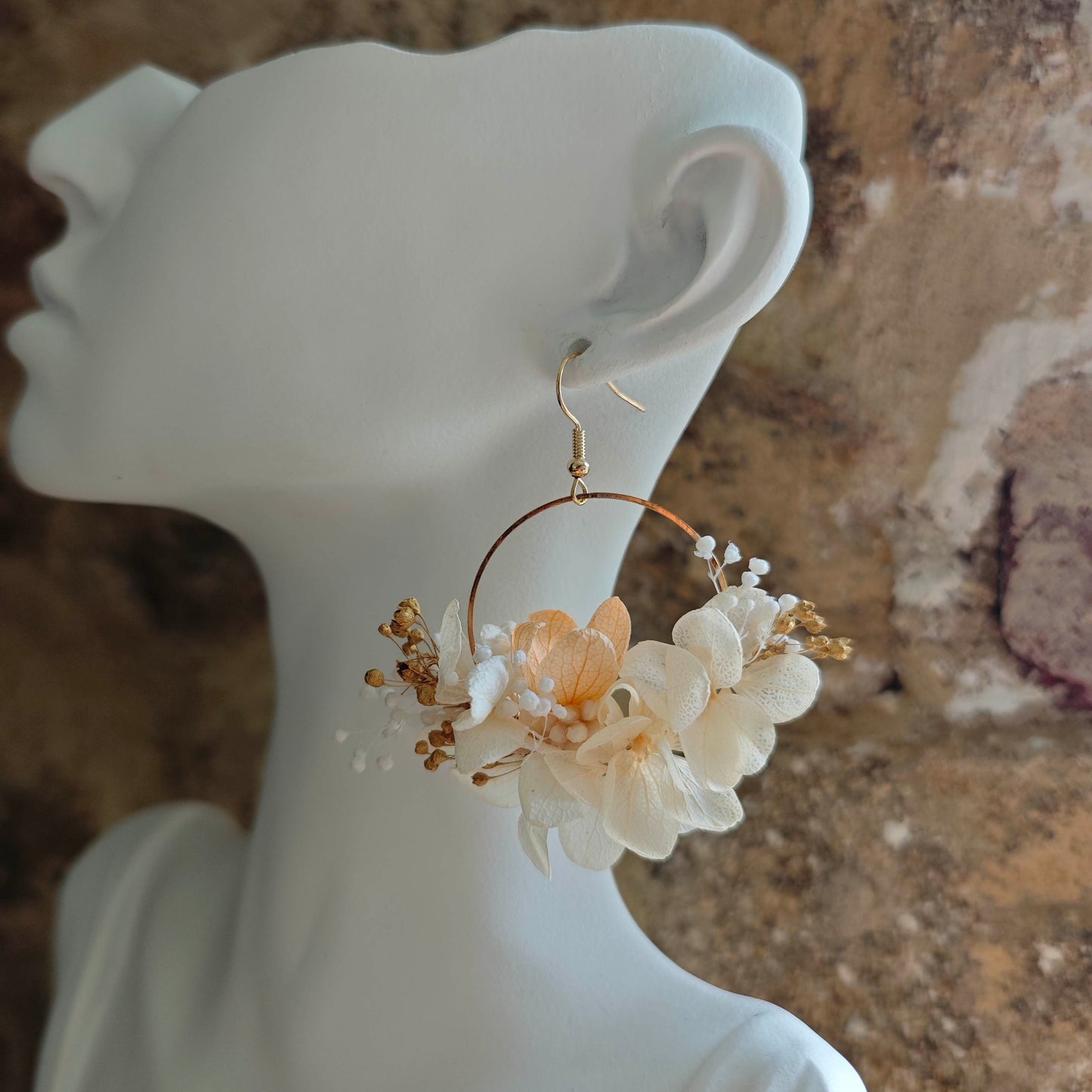 Créoles florales blanches et dorées photographiées sur fond clair, ambiance douce