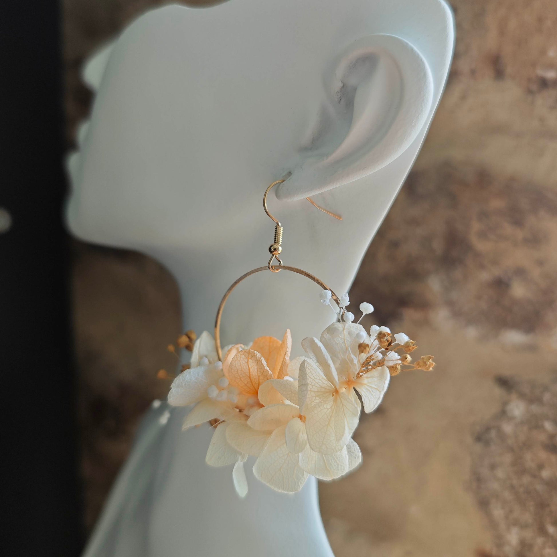 Boucle d’oreille créole faite main, fleurs séchées blanches et champagne portée sur un buste blanc