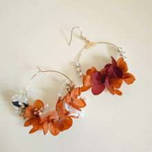Charger l&#39;image dans la galerie, Paire de boucles d’oreilles créoles faites main, ornées de fleurs séchées orange, blanches et bordeaux, avec perles blanches sur un fond beige.

