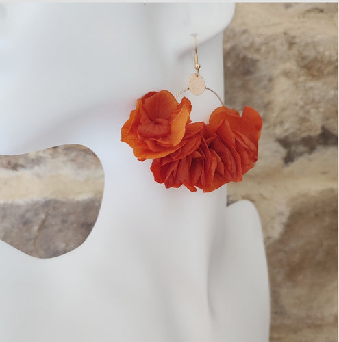 Boucles d'oreilles Léna avec fleurs stabilisées orange et métal doré, présentées sur un buste noir et blanc.