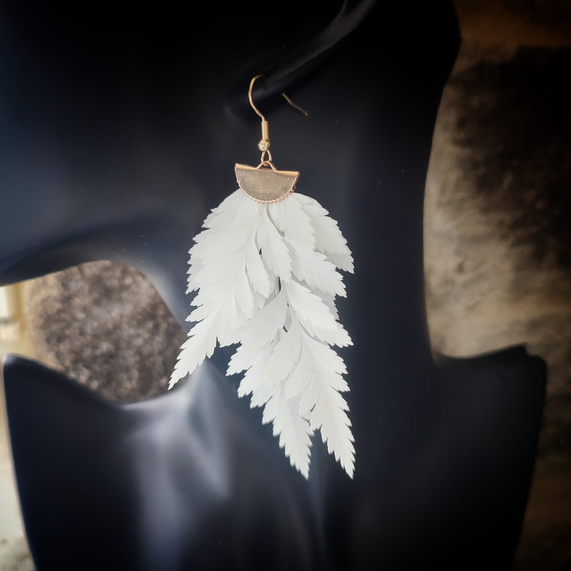 Vue rapprochée d'une boucle d'oreille en fougère stabilisées et séchées, mettant en valeur les détails des feuilles naturelles et le crochet en métal doré.