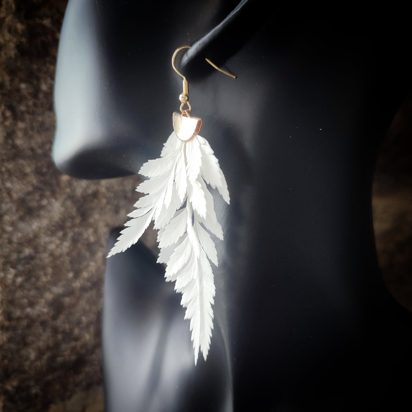 Vue rapprochée d'une boucle d'oreille en fougère stabilisées et séchées, mettant en valeur les détails des feuilles naturelles et le crochet en métal doré.