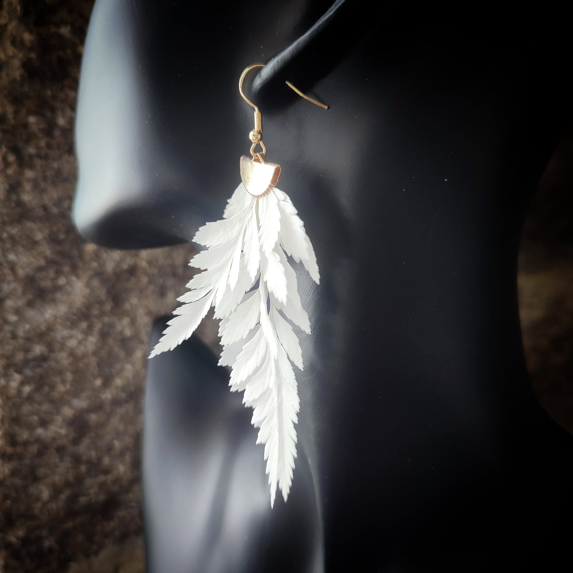 Vue rapprochée d'une boucle d'oreille en fougère stabilisées et séchées, mettant en valeur les détails des feuilles naturelles et le crochet en métal doré.